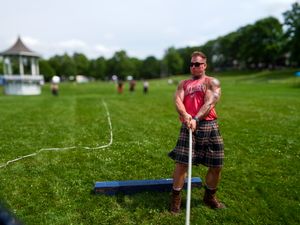 Competitor preparing for weight throw event at Highland Games on grass field with tents visible.