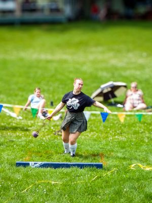 Athletic competitor in kilt performing dynamic throwing movement on grass field with colorful flags.