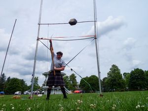 Weight over bar competition at Highland Games showing throwing technique against blue sky.