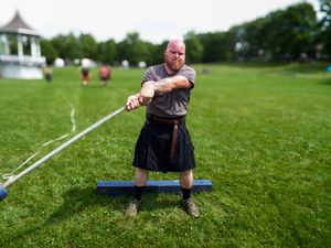 Side view of Highland Games weight throw competition with athlete in traditional Scottish dress.