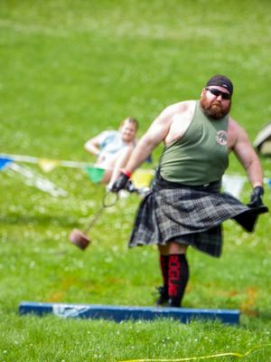Competitor in kilt performing athletic throw during Highland Games competition on grass field.