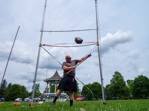Highland Games weight over bar event showing throwing technique against cloudy sky.