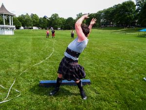Competitors practice weight throwing techniques at a Highland games event in a grassy park setting.
