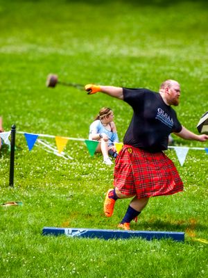 A participant in a red plaid kilt performs a weight throw during Highland games competition.