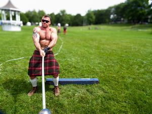 Competitors practice weight throws at a Highland games event on a sunny summer day.