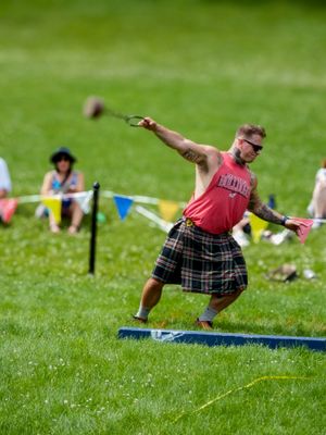 Athletic competitors perform weight throwing events wearing traditional kilts at Highland games.