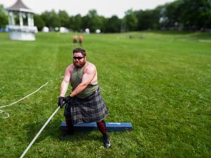 Athletes compete in traditional Scottish highland games on a grassy field with a white gazebo in the background.