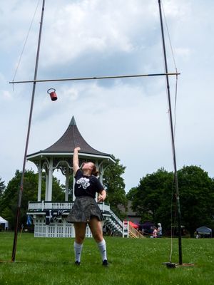 Competitors prepare for a weight throw event at a Scottish highland games competition on a sunny day.