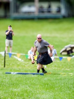 Participants compete in weight throwing events at a Scottish festival on grass field.