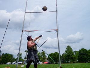 Competitor throws weighted object over high bar during Scottish highland games competition.