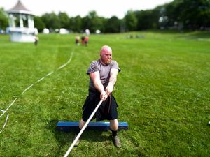 Athletes practice throwing techniques during Scottish highland games on sunny afternoon.