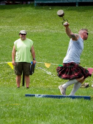 Athletes training with weighted implements on a sunny lawn during Highland Games practice.