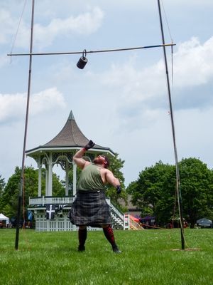 Highland Games weight throw practice showing sequential motion against blue sky and gazebo.