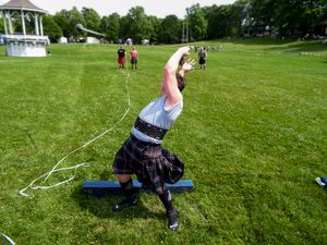 Athletes training for Highland Games events on grass field with gazebo visible.