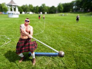 Athlete in plaid kilt practices hammer throw technique during Highland Games competition.