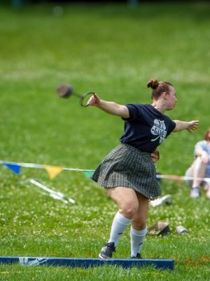 Athletic competitor in traditional Scottish kilt performs hammer throw technique on grassy field.