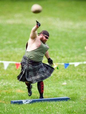 Competitor in traditional Highland dress performs hammer throw sequence on grass field.
