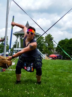 Competitor performs hammer throw at Highland Games with gazebo visible in distance.
