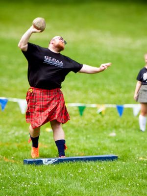 Athlete in traditional Scottish attire demonstrates hammer throwing technique at outdoor event.