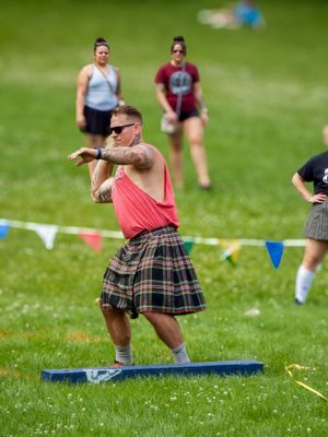 Athletes compete in traditional Scottish games wearing kilts while throwing objects on a grassy field.