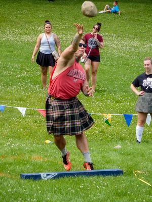 Competitors in kilts participate in field events at a Highland games competition on grass.