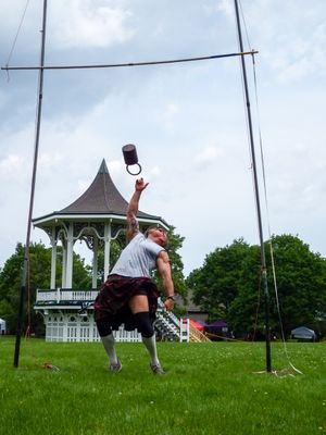 Highland games athlete performs weight throw against backdrop of white gazebo.