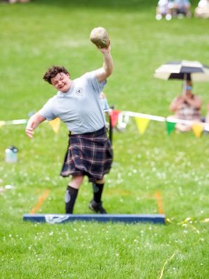 Competitor in traditional Scottish attire practices throwing technique on grass field.