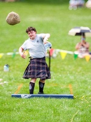 Highland games participant in kilt prepares to throw during competition on grassy field.