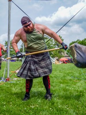 Competitor in traditional Highland dress performs throwing technique during games.