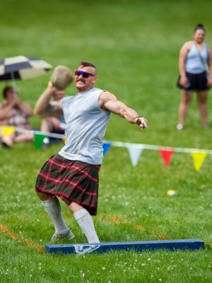 Athletes compete in traditional Scottish field events on grass with colorful flags.