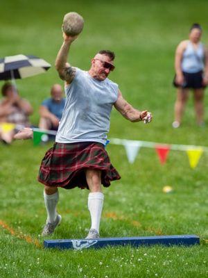 Competitor in kilt and gray shirt performs throwing technique during Highland games.