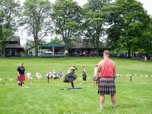 Wide view of a Highland Games field with spectators watching athletic events on a sunny day.