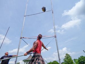 Action sequence of a weight throw competition at Highland Games with vertical poles marking the field.