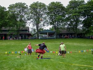 Panoramic view of a Highland Games event field with competitors and spectators on a grassy lawn.