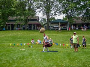 Traditional Highland Games competition takes place on a sunny day with spectators watching.