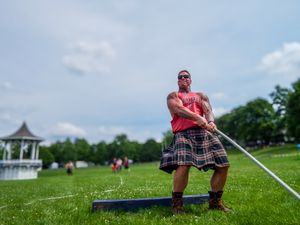 Competitor in traditional Scottish kilt throws hammer at Highland Games competition with gazebo in background.