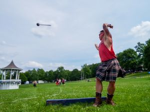 Athletic participant in plaid kilt practices hammer throw technique at outdoor Highland Games event.