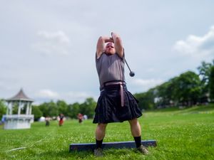 Highland Games athlete in dark kilt prepares to release hammer throw on grassy field.