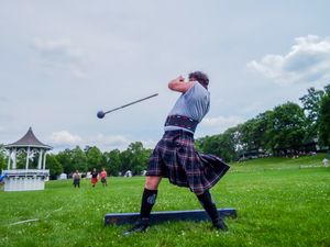 Athletic competitor performs hammer throw technique at Highland Games with white gazebo in background.