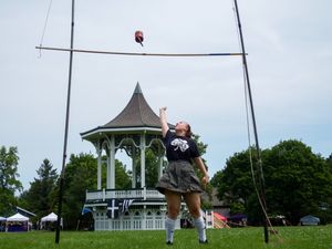 Highland Games participant attempts high jump near decorative gazebo during competition.