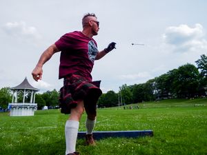 Highland Games athlete in maroon shirt performs hammer throw stance on platform.