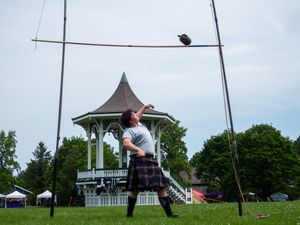 An athlete in a kilt practices weight throwing at a park with a white gazebo in the background.