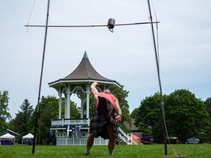 An athlete attempts a high weight throw during Highland Games with a gazebo in view.