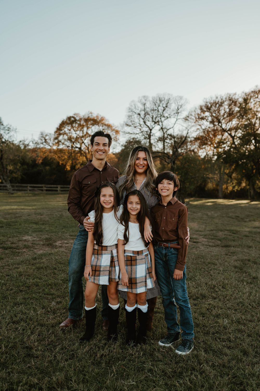 Family of five posing in a field during fall, wearing coordinated brown and plaid outfits with boots.