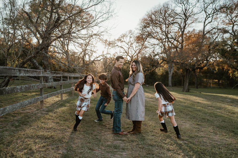 Family of five walking and laughing together in a rustic field with wooden fence and autumn trees.