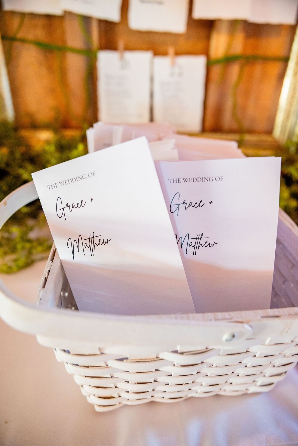 Wedding programs for Grace and Matthew displayed in a white wicker basket at the ceremony.