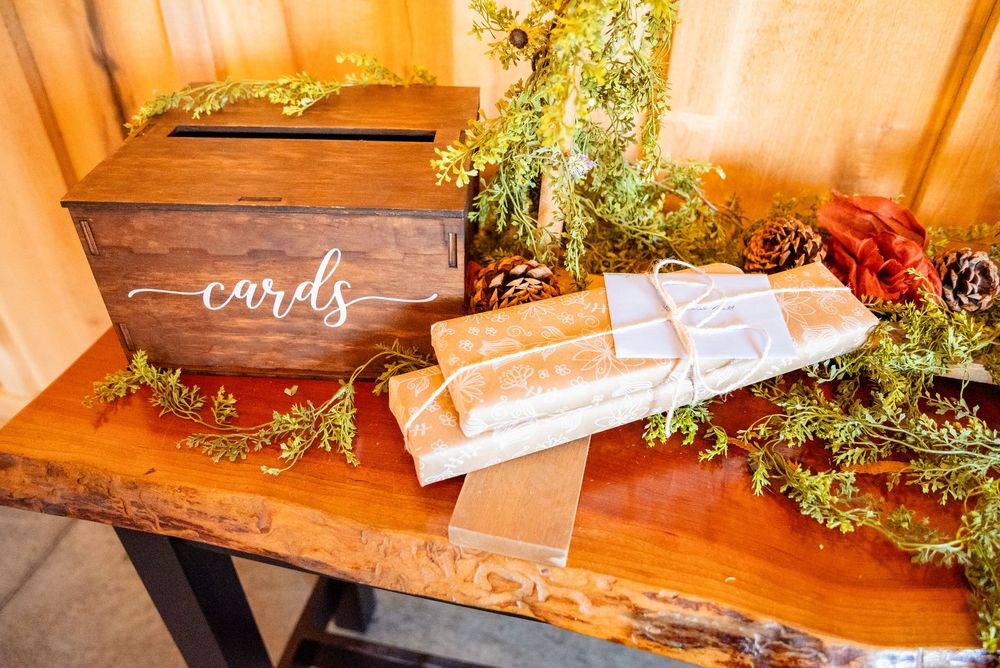 Rustic wooden wedding card box surrounded by autumn greenery, pine cones, and wrapped gifts on a wooden table.