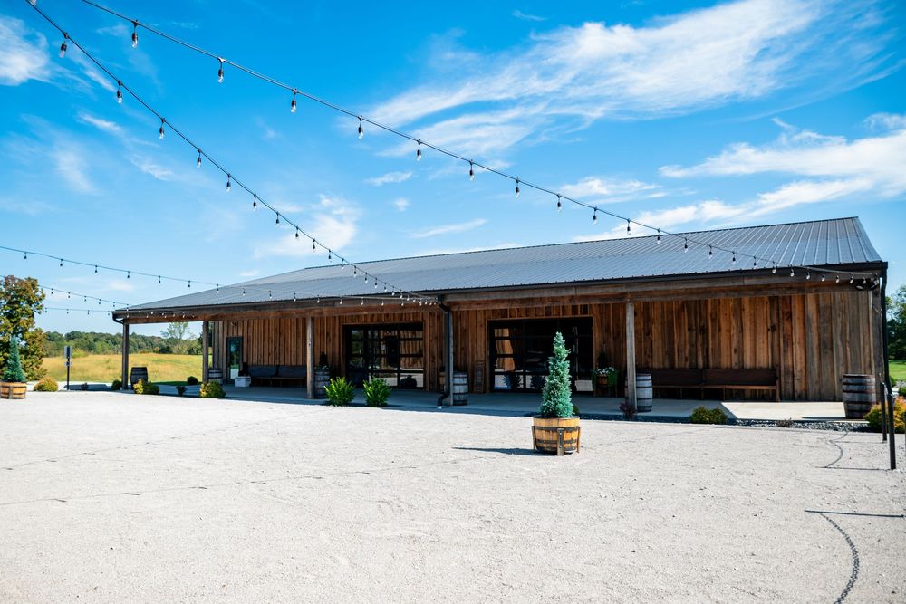 Rustic barn wedding venue exterior with string lights and blue sky on a sunny day.