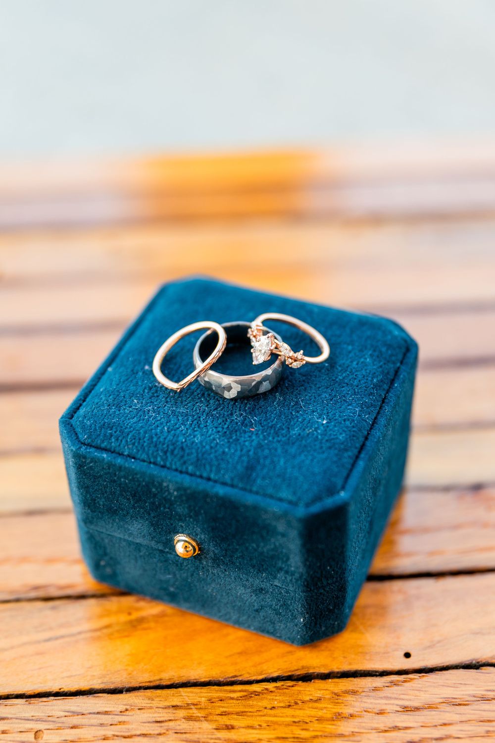 Three wedding rings displayed on a blue velvet jewelry box on a wooden surface.