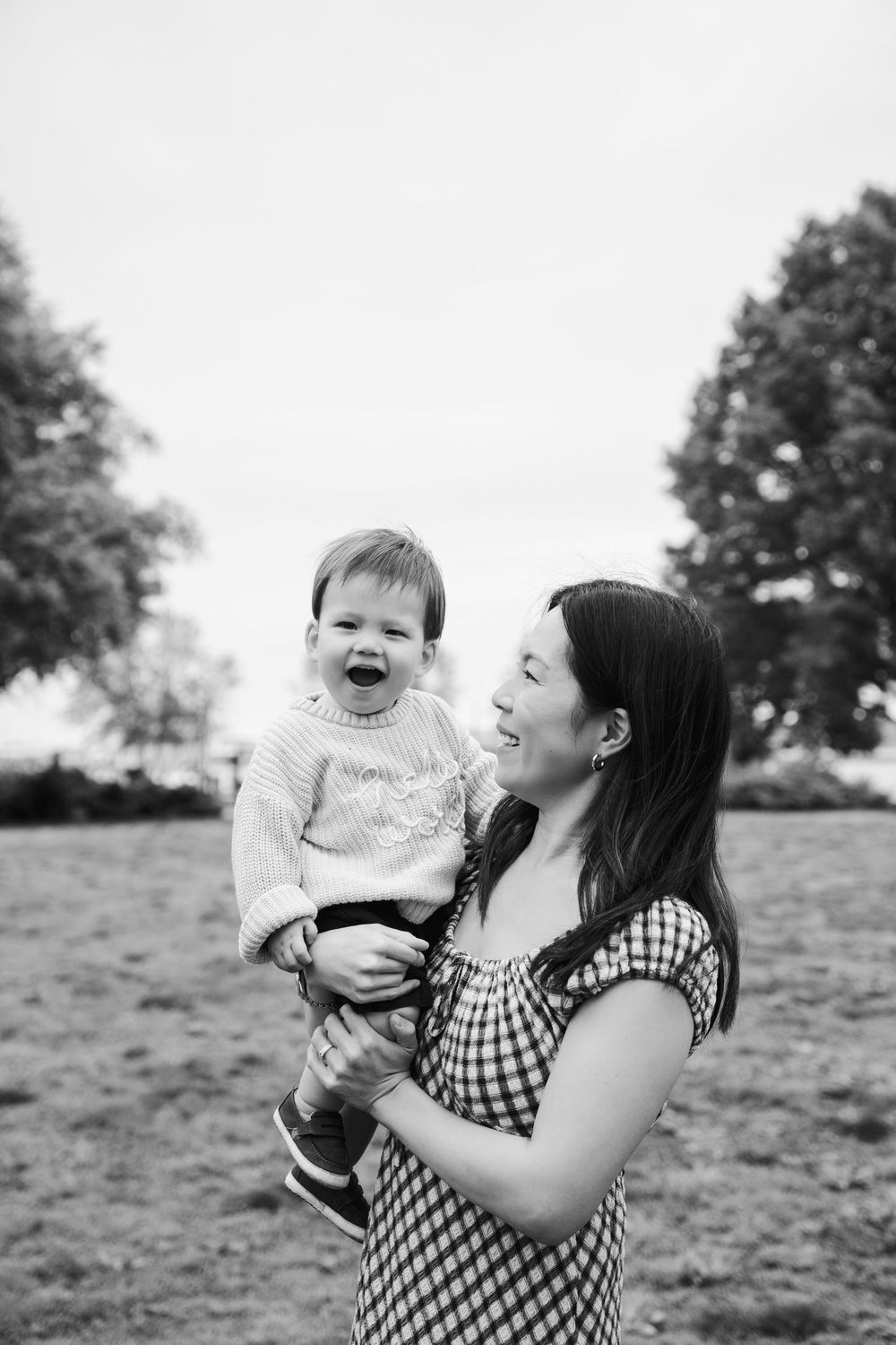 A joyful mother holds her laughing toddler in a black and white outdoor portrait in a park.